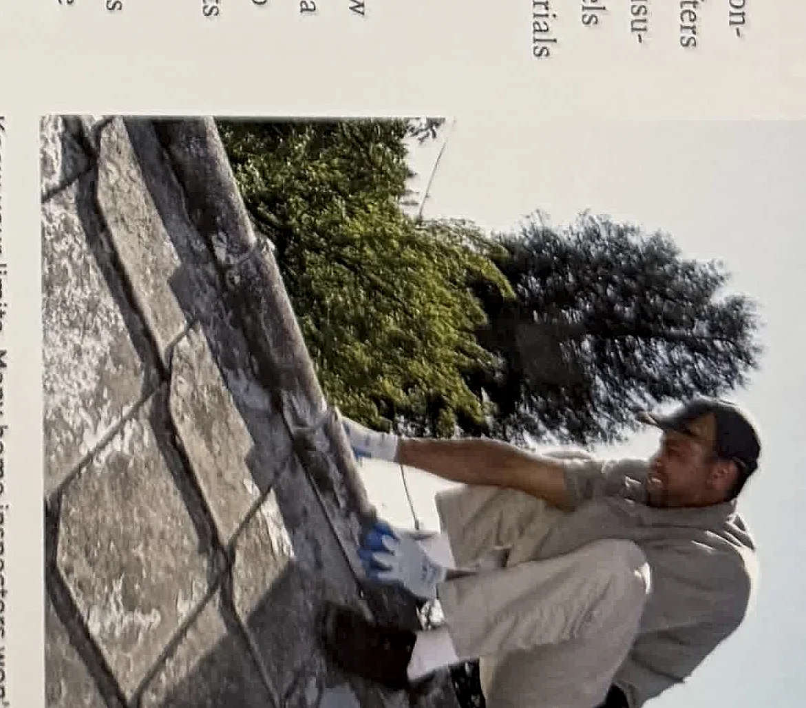 A cropped textbook photo of an inspector evaluating roof conditions from a ladder or roof edge.
