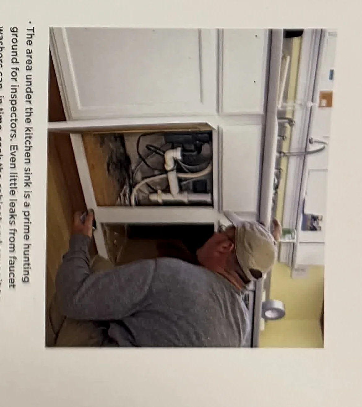 A cropped textbook photo of an inspector checking plumbing or cabinet conditions.